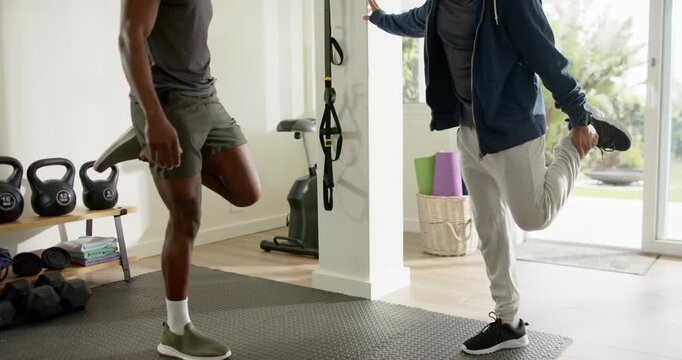 Male trainer guiding trainee through leg stretch mirroring and improving flexibility at home gym