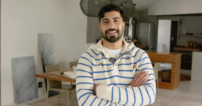 Indian man in hoodie facing camera in kitchen, reacting to camera with smile broadening into laugh
