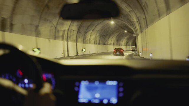View from inside a car driving through a dark tunnel and emerging onto a lit highway. Concept journey and transition from enclosed space to open road
