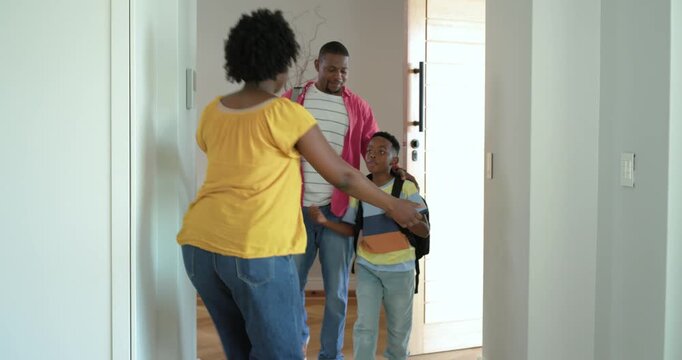 African American family entering home, dad opening door, mom hugging school-age son after school