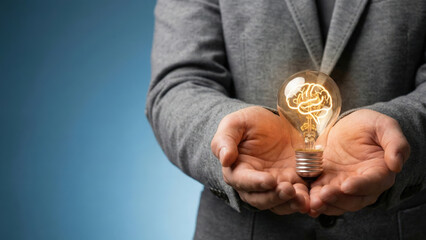 Creative idea concept with glowing light bulb shaped like brain held by person in gray suit jacket, symbolizing innovation and intelligence