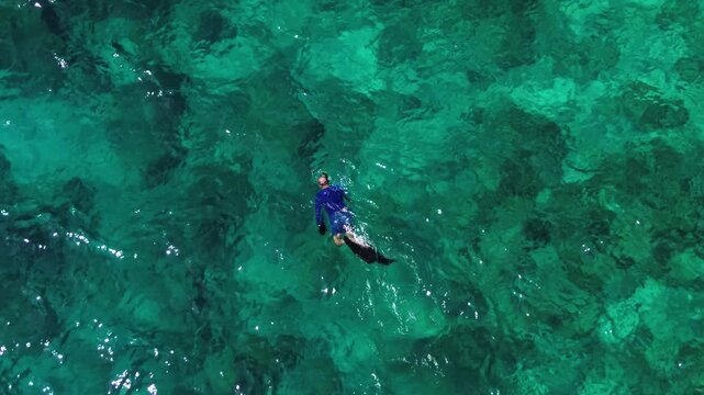 Vacation in Southeast Asia, sea travel in Thailand. Snorkeling near tropical islands. A man exploring the underwater world off the coast of Racha Yai Island, as seen from a drone.