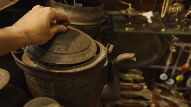 Hand Examining Antique Metal Kettle and Artifacts in Souk Shop