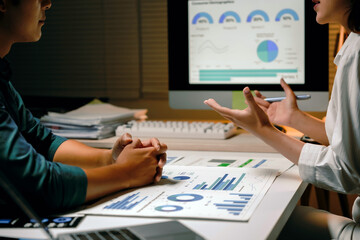 Business team discussing financial data and charts on computer screen and documents. Working late in modern office