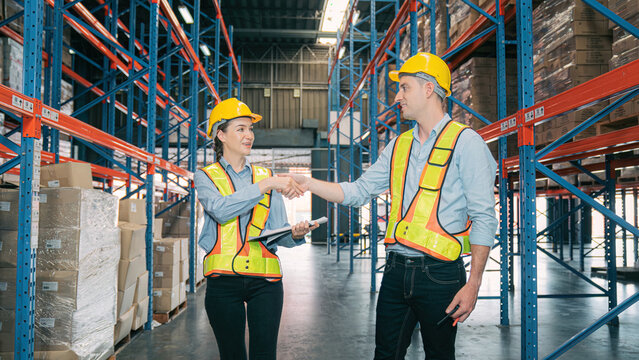 Confidence caucasian man, woman staff worker wear safety helmets, vest handshake teamwork collaborate, cooperation in logistics inventory operation. show success,efficiency modern warehouse management - Powered by Adobe