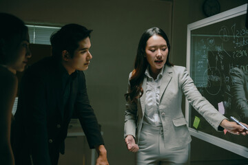 Asian business professionals discussing ideas and strategy, drawing diagrams on a whiteboard during a late night meeting