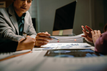 Business professionals collaborating and discussing financial statistics, charts, and graphs in a late night office meeting