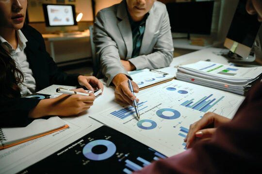 Business professionals collaborating and discussing company financial data, charts, and reports on a table in an office late at night