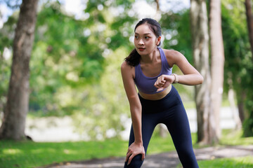 Woman pausing during run, checking fitness progress on her smartwatch in a green park, focusing on health and active lifestyle