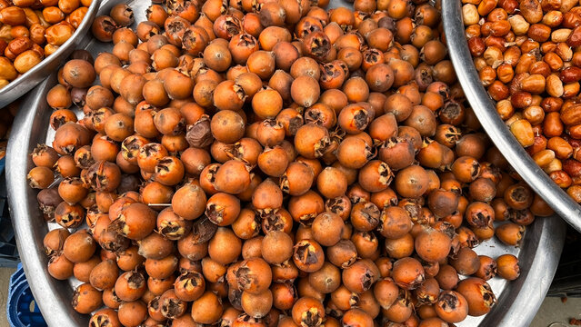 Close-up view of ripe persimmons (mushmula) displayed in a large metal tray. Local market and seasonal produce.