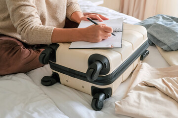 Travel planning scene with carry-on suitcase used as desk, open notebook and smartphone, hands...