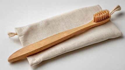 a natural bamboo toothbrush lies horizontally across a beige fabric pouch on a clean white surface