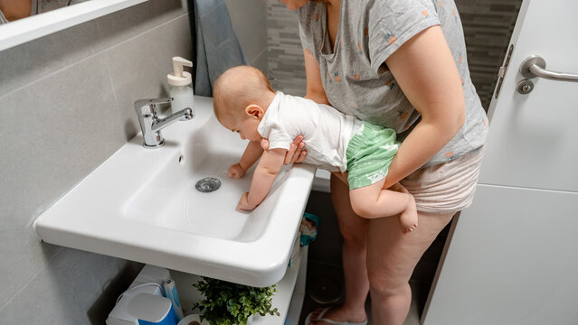 Baby exploring sink with adult supervision