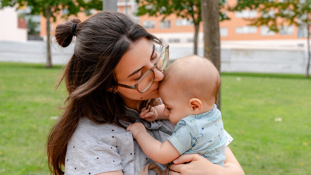 Mother kissing baby in park on a sunny day