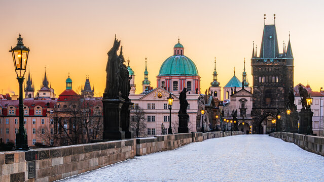 The UNESCO world heritage site Charles Bridge covered in snow with shining lamps in Prague in the winter morning dawn. 