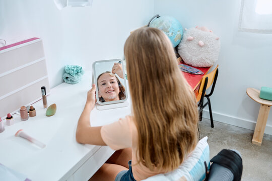 Teenage girl applying makeup at home vanity