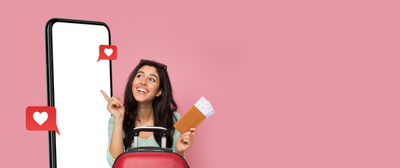 A young woman joyfully poses with her travel suitcase, smartphone, and travel documents. The bright...