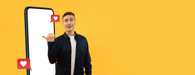 A young man stands next to a large smartphone with a cheerful expression, showcasing social media reactions. The bright yellow background adds energy, creating a lively scene focused on connectivity.