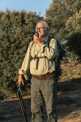 Senior hunter communicating on walkie talkie while holding shotgun
