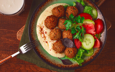 Healthy meal with falafel, tahini, salad, and drink on wooden table in cozy setting at lunchtime