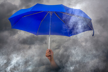 Blue Umbrella Held Up Against Dramatic Dark Storm Clouds with Fog