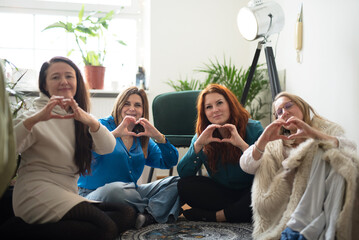 Group of women sitting indoors and make report on internet showing heart from hands. Relationship of best friends during fun and meeting . Adult people.