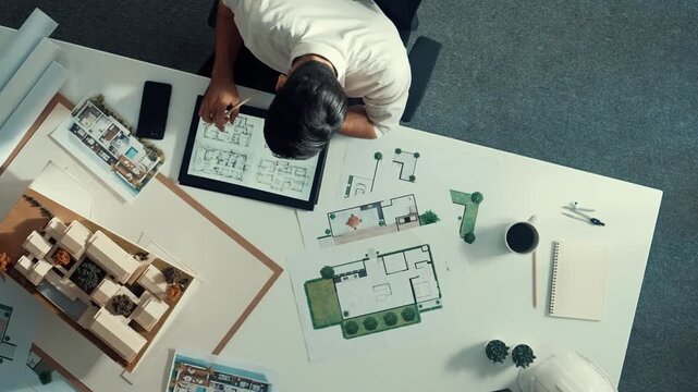 Top view of business man using tablet plan house design while sitting at meeting table with blueprint and equipment scatter around. Aerial view of civil engineer working at blueprint. Alimentation.