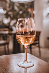 White wine in a elegant glass, resting on a rustic wooden table in a dimly lit restaurant or bar with bokeh background