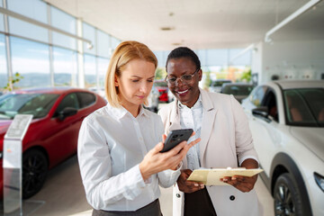 Salesperson and customer using phone in car dealership
