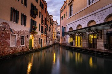 Naklejka premium Evening in Venice - calm surface of a small canal between houses with reflection of lights on the surface