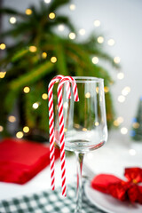 Holiday wine glass decorated with two red white candy canes. A festive background with Christmas lights and seasonal table elements. Close-up. Selective focus.