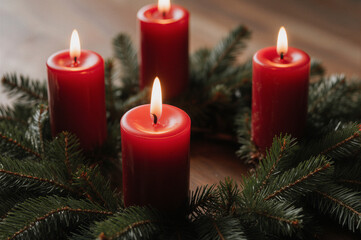 Four red candles burning warmly surrounded by greenery, evoking a festive and cozy atmosphere.