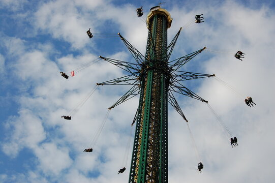  People enjoy the high swing ride at Prater amusement park on a sunny day. The spectacular star-shaped Prater Tower (Praterturm) offers excitement and adventure.
