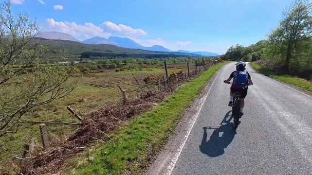 active senior woman riding her electric mountain bike along the Caledonian Canal near Fort William with Ben Nevis summit in background, Scotland, UK
