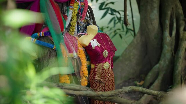 Scary Thai Traditional Dresses Hanging on Sacred Tree, The atmosphere represents Thai superstition, animism, local beliefs, and the mystery of spirits or ghosts associated with lottery luck and worshi