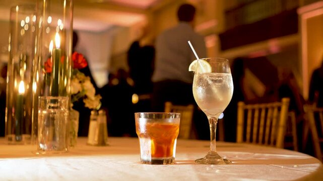 alcoholic drinks on table at a wedding reception party during the night with dancing people in the background