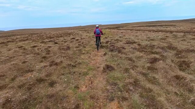 active senior woman riding her electric mountain bike on the moor landscape of Rua Reidh point near Gairloch in Scotland, UK