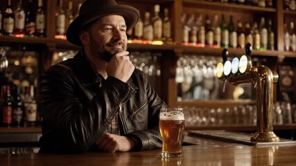 Rugged man with a beard sits at a rustic bar counter, clad in a stylish leather jacket. He enjoys his own company, sipping on a frothy pint of beer with a contemplative expression