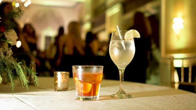alcoholic drinks on table at a wedding reception party during the night with dancing people in the background