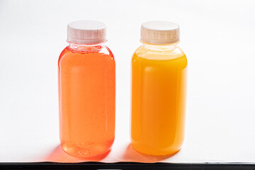 Two vibrant drinks stand in clear bottles, showcasing rich hues of orange and pink