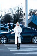 Elegant woman crossing the street in a stylish white coat, as cars patiently wait at the zebra...
