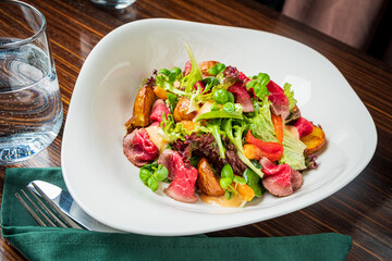 A vibrant salad featuring greens, roasted vegetables, and savory meat presented on a stylish dish