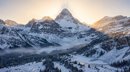 Obraz premium Snow-covered mountain peak rises above frozen lake and pine forest. Golden sunlight illuminates the summit creating a serene winter atmosphere. Ideal for travel and nature concepts.