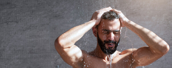A man stands under a warm shower, water cascading around him. He appears relaxed, enjoying the...