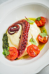 Enjoy grilled octopus on creamy mashed potatoes with fresh herbs and roasted tomatoes
