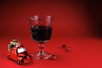 Glass of red wine standing with toy car full of presents and festive bells creating joyful holiday mood