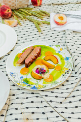 A picnic feast presents exquisite duck breast artfully arranged with fresh peach slices and flowers