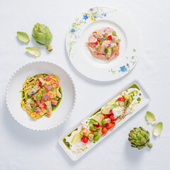 A lovely table displays colorful dishes, fresh pasta, and artichokes in soft lighting