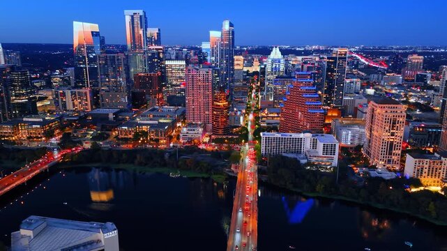 Flow of cars with headlights on moves by the bridge over the Colorado River. Fantastic scenery of Austin downtown, Texas, USA with colorful illumination.
