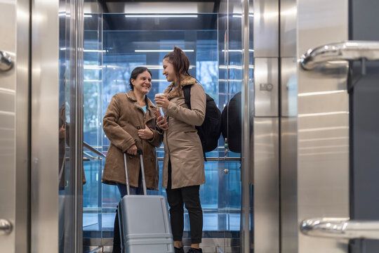 Two women traveling and conversing in modern elevator - Powered by Adobe